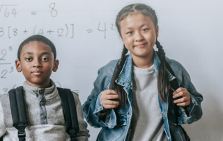 two kids with backpacks on in front of whiteboard